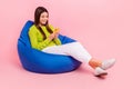 Full length photo of cute young girl sitting blue bean bag reading news wifi dressed stylish green look isolated on pink Royalty Free Stock Photo