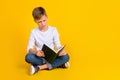 Full length photo of doubtful unsure boy wear white shirt reading book empty space isolated yellow color background Royalty Free Stock Photo