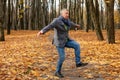 Full length photo of energetic aged man dancing on path in golden forest. Fallen dry yellow maple leaves everywhere.