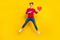 Full length photo of excited cute young guy dressed red pullover pointing finger red heart jumping isolated yellow color