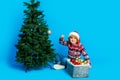 Full length photo of excited funny little boy dressed ugly pullover x-mas hat hanging baubles isolated blue color