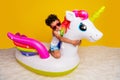 Full length photo of funky cheerful small boy wear white shirt riding floating unicorn matrass isolated yellow color