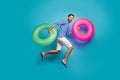 Full length photo of funky crazy guy tourist jump high running swimming hold two colorful lifebuoys circles wear striped