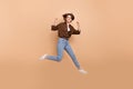 Full length photo of funky lucky lady wear brown shirt jumping high rising fists  beige color background Royalty Free Stock Photo