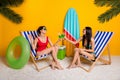 Full length photo of funky sexy girls dressed swimsuits sitting lounge chairs cheering alcohol cocktails isolated yellow