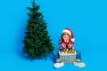 Full length photo of funny dreamy little boy dressed ugly pullover x-mas hat hanging baubles isolated blue color