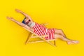 Full length photo of funny pensioner wearing striped swimwear chilling lying sunbed at the beach isolated on yellow