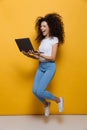 Full length photo of funny woman 20s wearing casual clothes smiling and jumping while holding black laptop, isolated over yellow Royalty Free Stock Photo