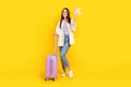 Full length photo of good mood woman dressed white jacket hold luggagge paper plane go on vacation isolated on yellow