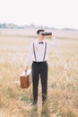 The full-length photo of the groom in vintage suit is carrying the old suitcase and looking through the binoculars in Royalty Free Stock Photo