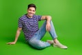 Full length photo of handsome cool optimistic man wear stylish t-shirt jeans sitting on floor smiling isolated on green Royalty Free Stock Photo