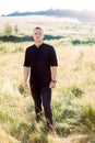 Full length photo of handsome young man in black shirt and pants, standing outdoor in the beautiful green summer field Royalty Free Stock Photo