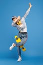 Full length photo of happy carefree young woman with yellow penny or skateboard and headphones dabbing over blue