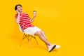 Full length photo of happy positive cheerful man talk phone hold coffee sit chair isolated on yellow color background Royalty Free Stock Photo