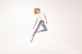 Full length photo of happy, smiling, young blonde girl in casual jeans and white t-shirt jumping, dancing over light studio Royalty Free Stock Photo