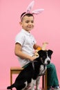 Full length photo of a little boy wearing bunny ears on head with basket ful of painted eggs sitting on a chair and a Royalty Free Stock Photo