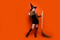 Full length photo of lovely blonde teen lady broom point empty space dressed black halloween garment isolated on orange