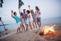 Full length photo of millennial guys ladies drink beer wear casual outfil by the ocean outside outdoors