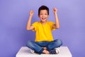 Full length photo of nice young pupil boy raise fists lucky sit white cube dressed yellow garment isolated on violet