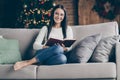 Full length photo of positive cheerful brown hair girl sit divan in house with christmas lights ornament read x-mas