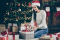 Full length photo of positive girl in santa claus hat sit floor carpet order christmas tree balls prepare for newyear Royalty Free Stock Photo