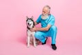 Full length photo of positive good mood old man dressed blue uniform stethoscope on neck pet husky on pink
