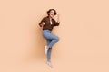 Full length photo of pretty excited girl dressed brown shirt jumping high rising fists empty space isolated beige color Royalty Free Stock Photo