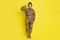 Full length photo of pretty focused girl standing arm near head saluting isolated on yellow color background Royalty Free Stock Photo