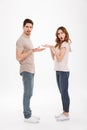 Full length photo of puzzled adult guy and girl wearing beige t-shirts standing face to face and gesturing on each other with