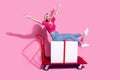 Full length photo of satisfied cheerful woman riding on shopping cart with large present raising arms up isolated on
