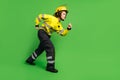 Full length photo of serious purposeful young firewoman dressed yellow uniform walking sneaking isolated green color