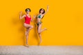 Full length photo of shiny lucky ladies wear bikini rising fists jumping high empty space isolated yellow color Royalty Free Stock Photo