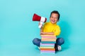 Full length photo of small cheerful boy sitting floor pile stack book hand hold loudspeaker isolated on cyan color