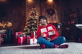 Full length photo of smiling handsome youngster arabian man sit carpet floor enjoying wrapped gift box indoors house