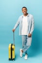 Full length photo of smiling young African-American guy in casual denim wear standing with yellow suitcase Royalty Free Stock Photo