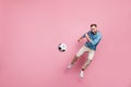 Full length photo of strong purposeful young man dressed blue sweater jumping high kick football ball isolated pink