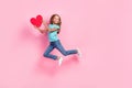 Full length photo of sweet adorable small kid wear turquoise t-shirt holding red heart jumping high pink color