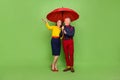 Full length photo of two carefree elegant aged people walk rainy weather isolated on green color background