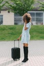 Full-length photo of the well-dressed afro-american woman holding the luggage while talking via the mobile phone.