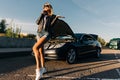 Full-length photo of woman standing in front of black car with open hood Royalty Free Stock Photo