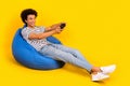 Full length photo of young addicted gamer guy lying bean bag joystick playing video games playstation isolated on yellow