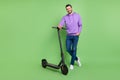 Full length photo of young cheerful man happy positive smile walk electric scooter isolated over green color background Royalty Free Stock Photo