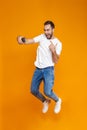 Full length photo of young guy 30s in casual wear laughing and taking selfie on cell phone, isolated over yellow background Royalty Free Stock Photo
