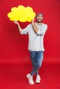 Full length photo of young man smiling and holding blank thought bubble isolated over red background Royalty Free Stock Photo