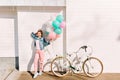 Full-length portrait of active cheerful girl with party balloons ready to bike ride in sunny morning. Stylish young Royalty Free Stock Photo