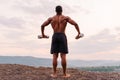 Full-length portrait of african american muscular athlete lifting dumbbells against the sunset sky background. Back view Royalty Free Stock Photo