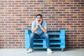 Full length portrait of amazed handsome young bearded man in casual style and eyeglasses sitting on blue wooden pallet and looking Royalty Free Stock Photo