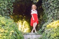 Full length portrait of attractive blonde young woman in stylish dress posing near floral arch in garden. standing and looking at Royalty Free Stock Photo