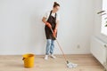 Full length portrait of attractive slim woman wearing white t shirt and apron posing with cleaning equipment and washing floor in