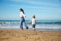 Full length portrait of Caucasian authentic family of a young mother and cute daughter running barefoot on the beach Royalty Free Stock Photo